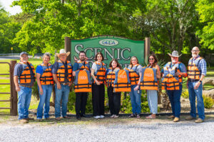 Cherokee County Farm Bureau members, Grand River Dam Authority Scenic River Operations staff and Tahlequah Area Chamber of Commerce staff stand with the new life jackets purchased for the 2025 float season.