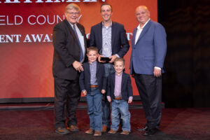 Oklahoma Farm Bureau President Rodd Moesel (left) presents Travis Schnaithman, along with sons Mack and McCoy, of Garfield County with the 2022 OKFB Young Farmers & Ranchers Achievement Award on Saturday, Nov. 12 at the 2022 Oklahoma Farm Bureau Annual meeting in Norman, OK. Also pictured is JJ Francais, assistant vice president of external affairs for Hilliary Communications, who sponsored the award.